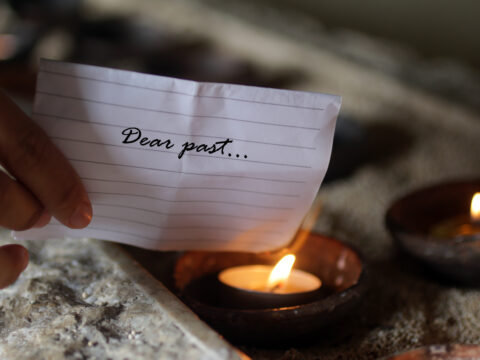 Vision, mission and values of Survive. This image shows a piece of paper, with the words, 'Dear past...' being held to a candle, signifying letting go of the past through counselling and support offered by Survive.